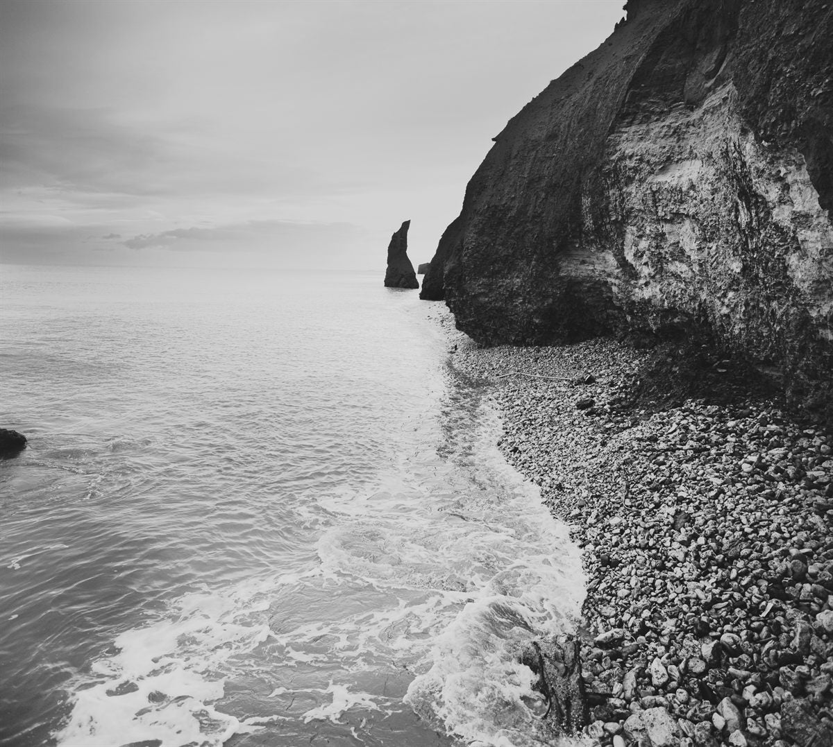 Surf meeting a pebble shore beneath a headland